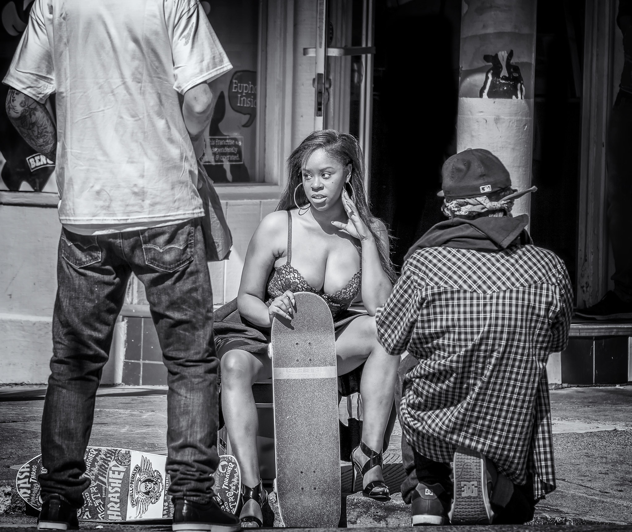Woman holds skateboard while seated, flanked by two men in San Francisco's Haight Ashbury district.
