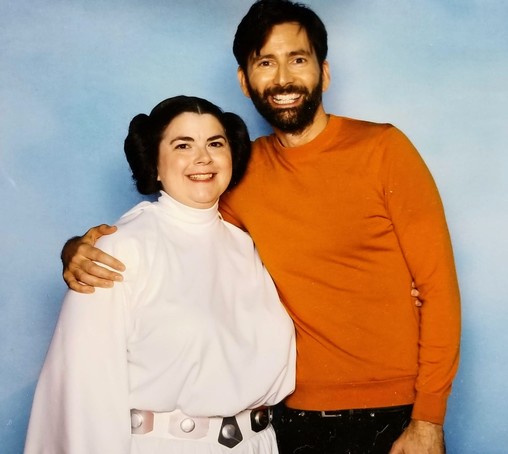 Woman dressed as Princess Leia is grinning from ear to ear while taking a photo with David Tennant, who also looks pretty happy.