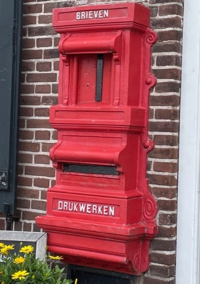 Red postbox against a brick wall in Veere, Zeeland, Netherlands.
Brieven = letters
Drukwerken = printed matters
The postbox looks historic, I do not know whether it's in use. 
On the left bottom side there are some yellow flowers
