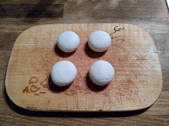 Four small sized white round cheeses laying on a wooden cuttingboard