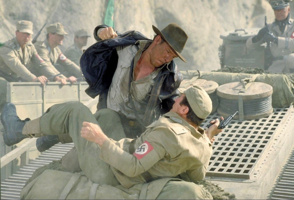 Screenshot aus Indiana Jones 1 der Indy zeigt,wie er neben einem auf dem Boden liegenden Nazi kniet und den verpruegelt. Im Hintergrund weitere Maenner in Naziuniformen