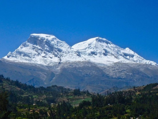 Dos montañas con la mitad superior nevada se alzan sobre una zona con bosques dispersos.