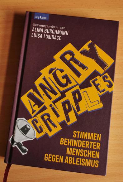 Das Buch Angry cripples" von Alina Buschmann und Luisa L'Audace auf einer Holzoberfläche 