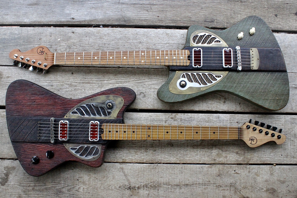 Two electric guitars laying flat on a weathered wooden floor. Both have the same jaunty body shape, with aluminum and brass hardware. One is red and black, the other green and brown.