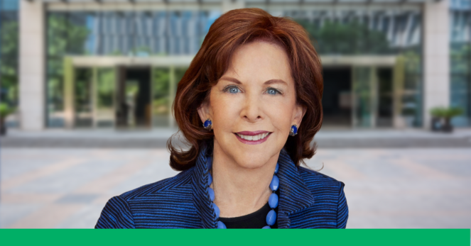 Posed headshot of Terry Savage, a middle aged woman with red hair and striking blue eyes. She stands in front of a steel-and-glass office building on Wall Street.
