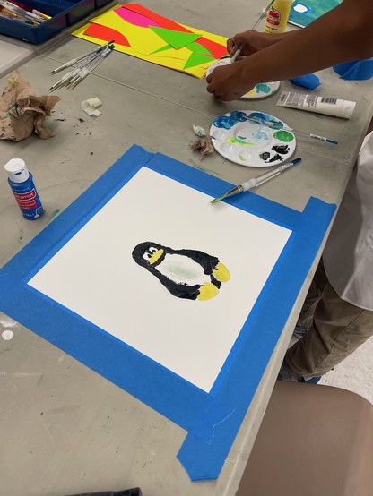 An acrylic painting of the Linux penguin, Tux, as painted by a student. Paintbrushes and paints can be seen.