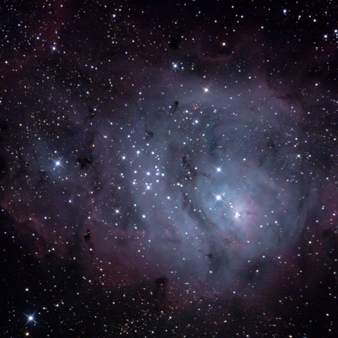 The lagoon nebula, seen here as a cluster of small bright stars amidst swirls of pale blue and pink clouds of interstellar gas and dust