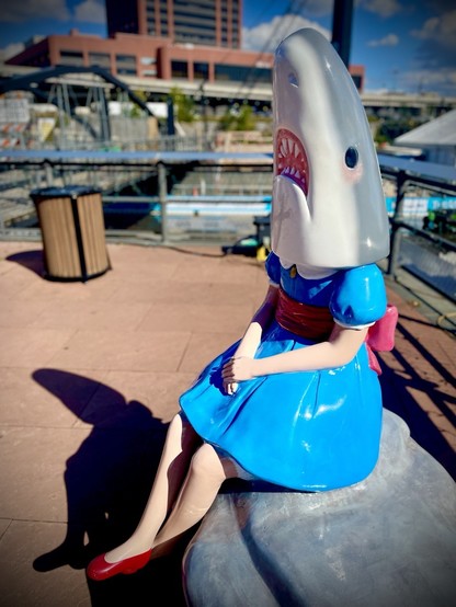 Statue of a girl in a blue dress with a shark head. 