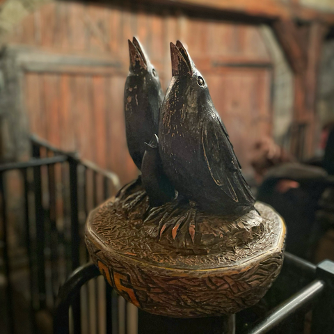 Close photo of crow decoration on station air gates of Flucht Von Novgorod roller coaster at Hansa-Park. They are made of metal and their beaks point upwards. Some of the blank coating is wearing off, revealing a bronze colour metal underneath.