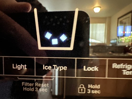 Close up of an ice type selector on a refrigerator dispenser. There is an “”Ice Type” button below a stylized image of a bucket containing ice cubes, which represents the current setting. 