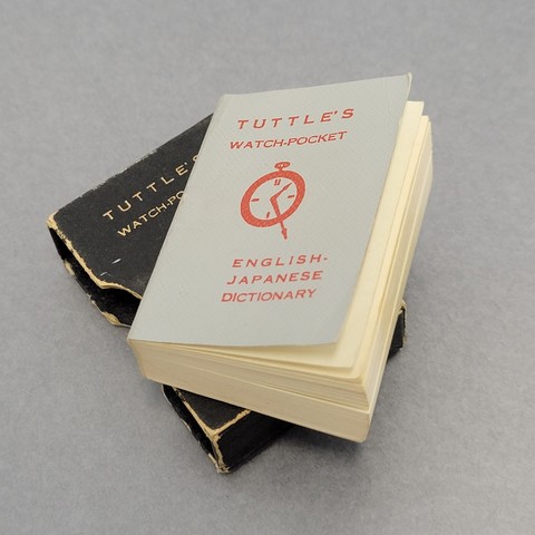 A tiny watch-pocket English-Japanese dictionary lying on its tiny cover box.