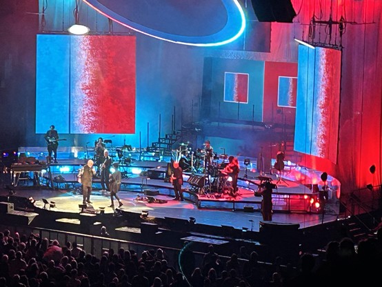 Zoomed in photo of the stage at a Peter Gabriel concert. The musicians are bathed in blue and red light.