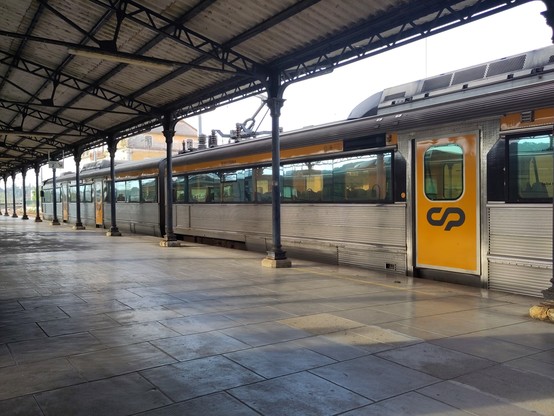 Seitenansicht eines Regionalzugs mit blanker Metallverkleidung und gelbem Türen im alten Bahnhof von Coimbra.