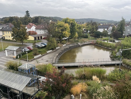 Regnerische Landschaft am Morgen mit Häusern und Bergen/Hügel, in der Bildmitte eine Wasseranlage, die wohl zum Hotel gehört.