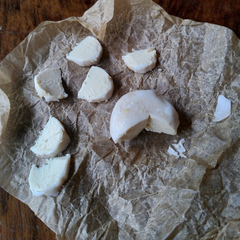 Partially cut soy cheese, with some light white/orange mold, laying on a sheet of baking paper