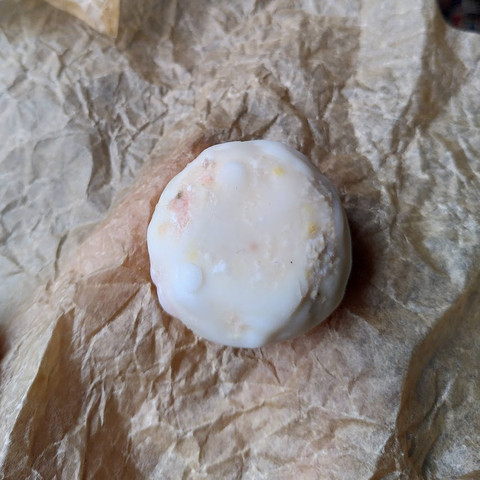 Whole soy cheese with some light white and orange mold spots, laying on a sheet of baking paper