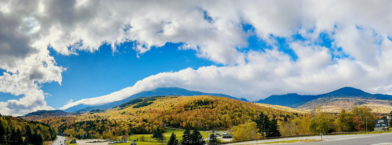Trees on Mt. Washington in New Hampshire changing colors in Autumn. Dramatic clouds in a blue sky above.  Wide Panorama photo. 