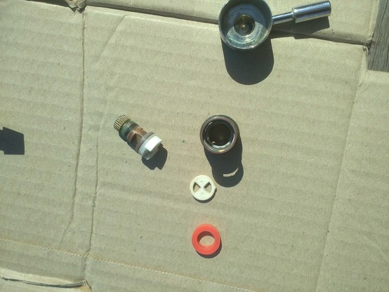 Cartridge disassembled showing annular washer, round ceramic (?) plate with two holes through it, and shaft with ceramic (?) plate transected by a groove on end of shaft.