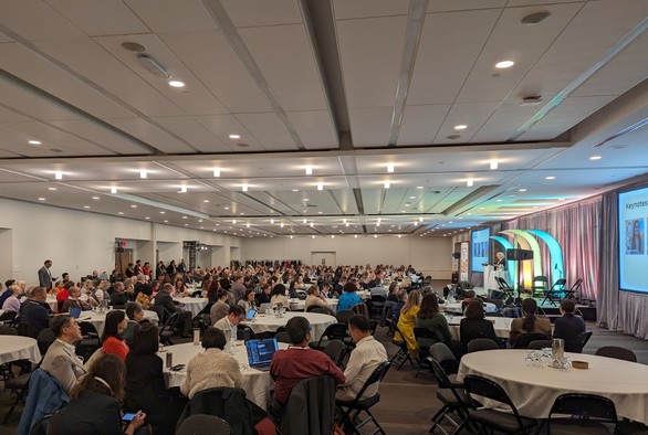 The OEGlobal 2023 main conference room with attendees listening to a keynote talk. 