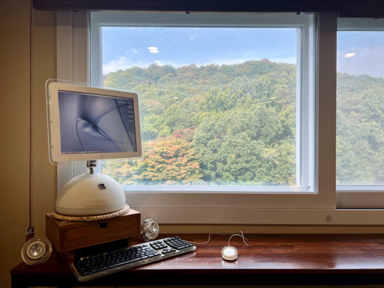 Photo of part of the bar (or tall side table) with iMac G4 standing on the left end, with a beautiful autumn-y view of trees and mountains through the windows behind t he bar.