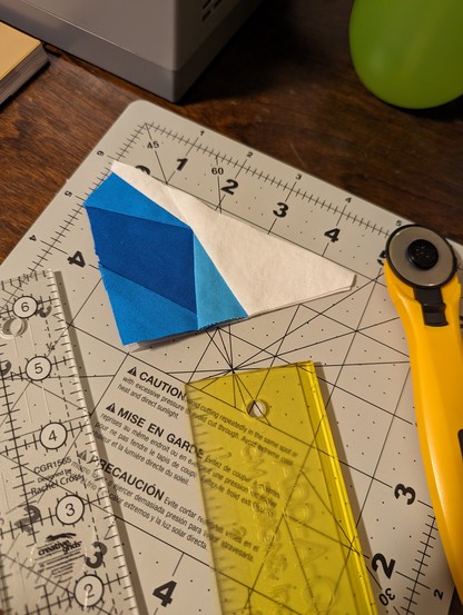 A blue &white quilted bit of fabric next to a few rulers and a rotary cutter, on a cutting matte. 