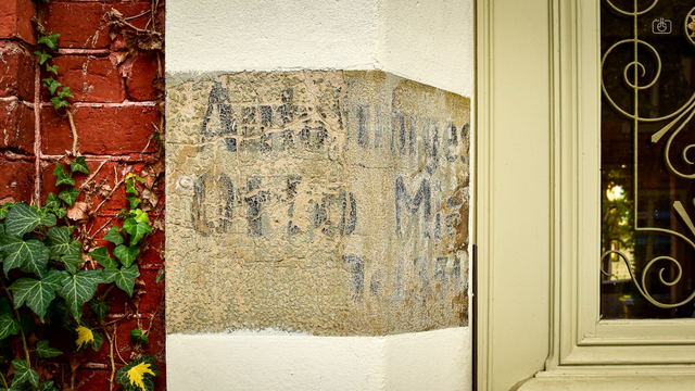 Ornate door with stone doorway and faded painted sign and red brick wall, Potsdam, 16 Oct 2023. Nikon D5600, Nikkor DX 35 mm ƒ1.8G, ISO 320, -0.3 ev, ƒ8, 1/100s