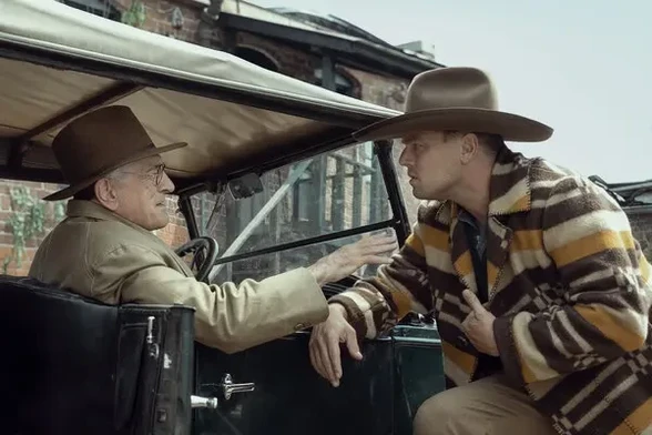 A movie still from Killers of the Flower Moon (2023). It shows Robert DeNiro sitting in his automobile and grasping Leonardo DiCaprio's arm.