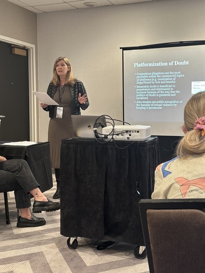Sarah Banet-Weiser standing at the front of a conference room speaking. A slide behind her is titled "Platformization of Doubt"