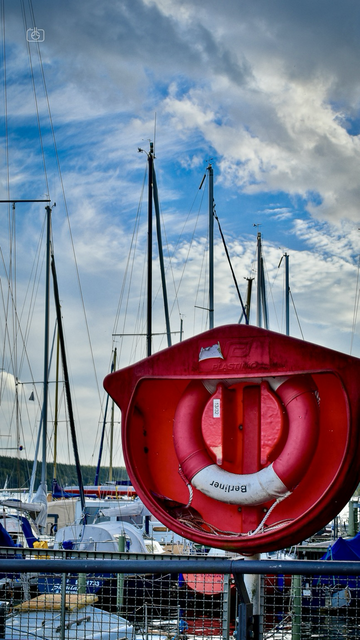 Lifesaver ring on stand in sailboat harbor in Havel River with sailboats moored in the background, Berlin-Kladow, 14 Oct 2023. Nikon D5600, Nikkor DX 35 mm ƒ1.8G, ISO 100, -0.3 ev, ƒ10, 1/100s