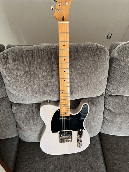 White squier telecaster relaxing a couch.