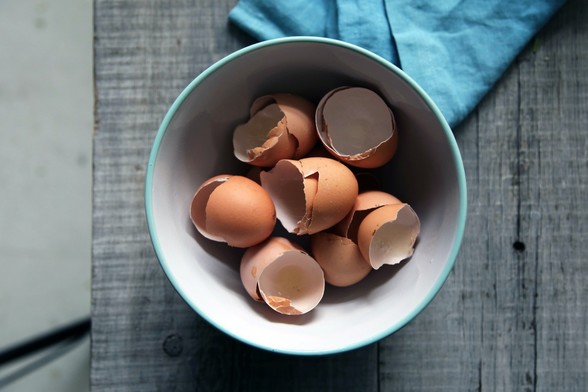 Top-view photo of brown eggshells in round white ceramic bowl on gray wooden board 