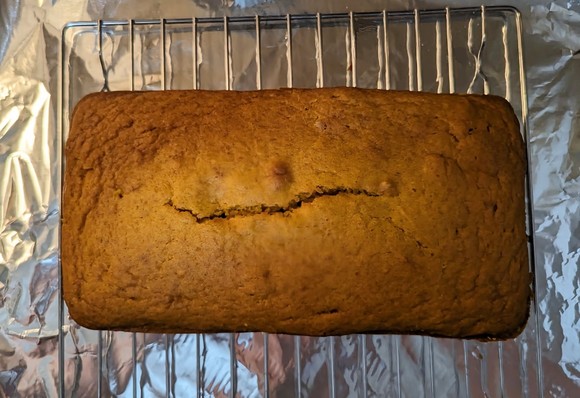 Pictured is a loaf of pumpkin bread on a cooling rack on a foil lined baking sheet.