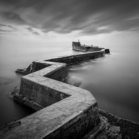 A B&W, long exposure photograph of the famous zig-zag breakwater at St Monans in Fife, Scotland. The view looks down the breakwater and out to sea.