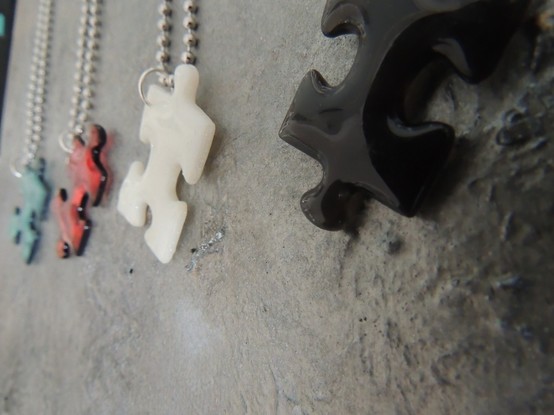 Puzzleteile aus Resin in blau, rosa, weiß und schwarz mit einer Kugelkette.