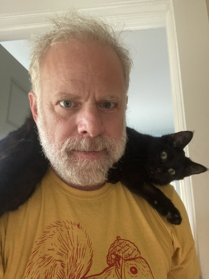 An adorable black cat lied across the neck and shoulders of an adorable middle aged man.
