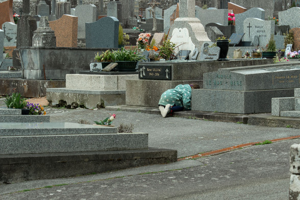 Un enfant accroupi entre les tombes d'un cimetière, bouinant on-ne-veut-pas-savoir-quoi