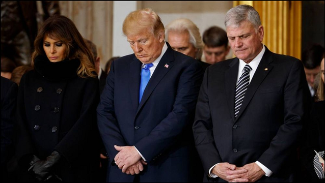 Dieses Foto zeigt von links nach rechts Melania Trump, Donald Trump und Franklin Graham, deren Köpfe zum Gebet geneigt mit geschlossenen Augen und gefalteten Händen dicht nebeneinander stehen und beten.