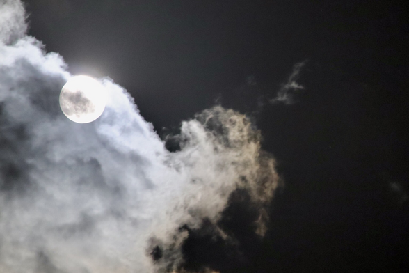 The bright disk of the nearly full moon to the right, partially obscured by a fluffy white cloud, with the tiny white dot of Uranus to the right, against a dark sky.