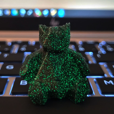 The Snorlax model printed in my own custom dual color filament. This is a photo, the model is sitting on my laptop, it is mostly black but has a lot of tiny glow in the dark particles lighting up in bright green. For more details check out the previous toot.