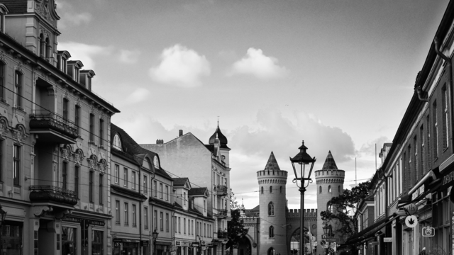To the left Italianate multistory buildings, to the right Dutch-style brick buildings, in the center Nauener Tor and a street lantern, Friedrich-Ebert-Straße, Potsdam, 16 Oct 2023