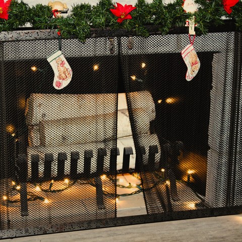 a cozy fireplace decorated with a green garland around the outside with four miniature stockings hanging in front. The fireplace has a pile of white birch logs and is lit with fairy lights.