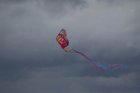 a colorful, mostly red, kite in the shape of a butterfly, in front of dark grey clouds