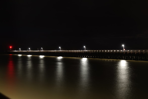 very long night exposure shot of a pier with white lights on top and a red light at the end, on the left side of the picture.