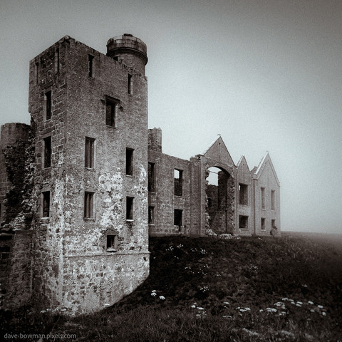 A monochrome, moody photograph of Slains castle ruin on a foggy day in Aberdeenshire, Scotland, UK.