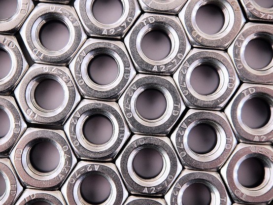 Photograph of a collection of hexagonal nuts, positioned in a clean, well-organized honeycomb pattern.