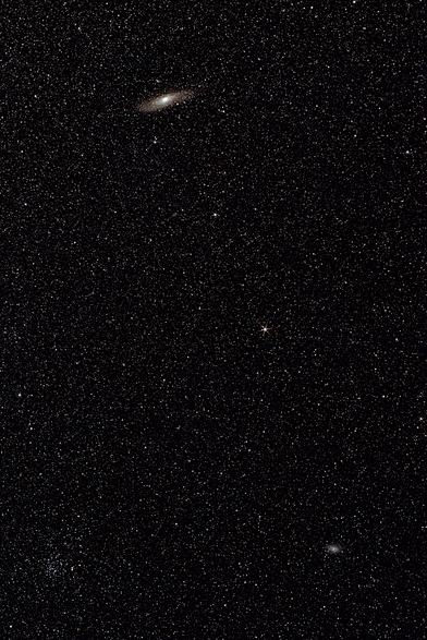 A field of tiny stars, with a few brighter ones, against a black background. At top is the Andromeda galaxy, seen as a small ellipse of swirling white. At lower right is the Triangulum Galaxy, similar, but considerably smaller and more compact. 