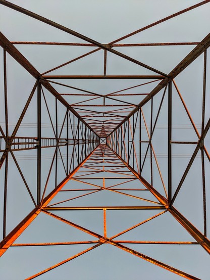 Color photo of Pylon/high tension tower looking up from the center of the base