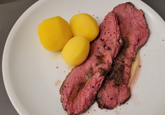 Farbfoto: Auf einem weißen Teller liegen zwei Scheiben des Fleischs, dazu drei Kartoffeln. Das Fleisch ist innen rosa, ein paar der Kräuter liegen darauf.
Es gab auch noch Salat dazu, aber der hat es nicht aufs Foto geschafft... 