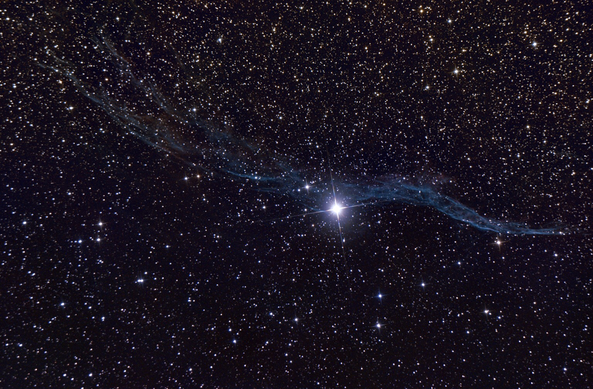 52 Cygni, a bright star near the middle of the frame, with four diffraction spikes, caressed by a long trail of thready, undulating wisps of blue, thinner and more concentrated to the right, and becoming more diffuse towards the left as it passes the star. All against a dark background peppered with small stars.