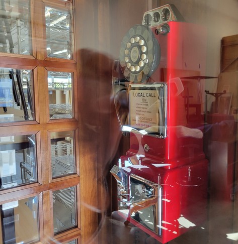 Interior phone of a stained wooden version of the red telephone box at an office furniture liquidation store. The phone is red with a rotary dial. Visible text says "Local call 10 ¢"